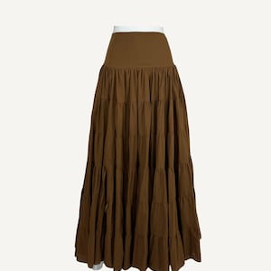 May include: A light brown tiered skirt with a high waist. The skirt is made of a flowing fabric and has multiple horizontal tiers, creating a full, flared silhouette. The text "Light Brown" is in the upper right corner.