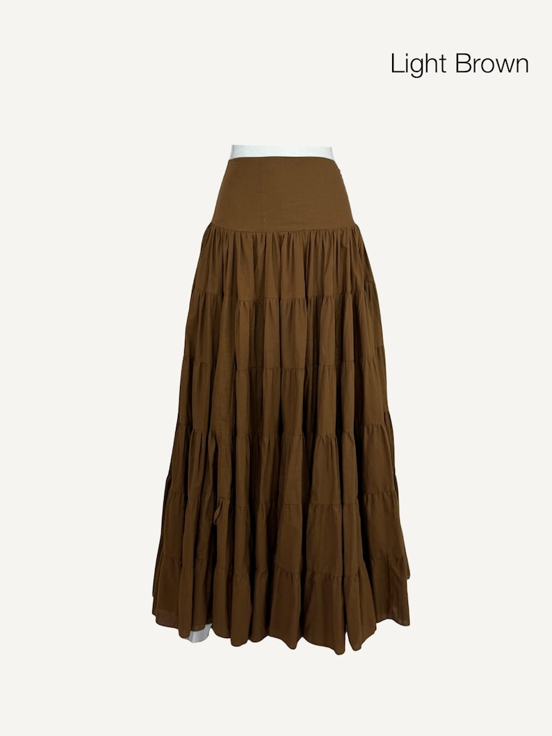 May include: A light brown tiered skirt with a high waist. The skirt is made of a flowing fabric and has multiple horizontal tiers, creating a full, flared silhouette. The text "Light Brown" is in the upper right corner.