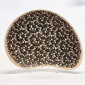 May include: A white ceramic serving dish with a brown lace pattern. The dish is shaped like a teardrop and has a slightly curved edge.
