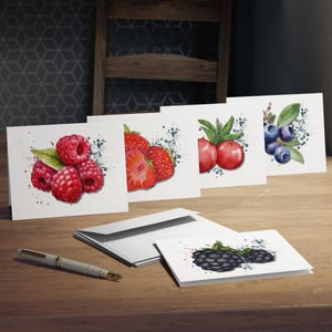 May include: A collection of greeting cards featuring watercolor illustrations of various berries, including raspberries, strawberries, blueberries, and blackberries. The cards are arranged on a wooden surface with a pen and envelopes.