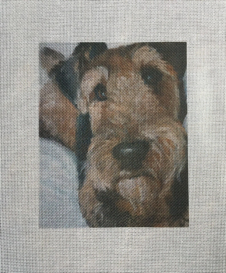 May include: Needlepoint canvas featuring a detailed portrait of a dog. The dog's fur is rendered in shades of brown and tan, with dark accents around the eyes and nose. The background is a soft, neutral color, and the canvas has a grid pattern.