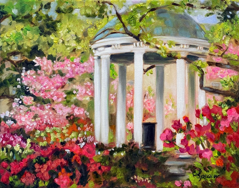 May include: A white, columned gazebo with a green roof surrounded by pink and red flowers. The gazebo is in a garden setting with green trees in the background.
