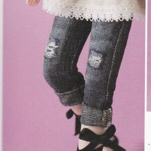 May include: A pair of dark blue denim jeans with distressed details and cuffed hems. The jeans are paired with black ribbon-tied shoes.
