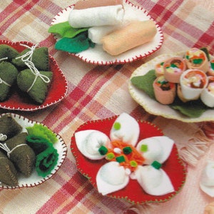 Op de afbeelding: Een verzameling van viltvoedsel, waaronder dumplings, loempia's en sushi, gerangschikt op verschillende borden. De voedingsmiddelen zijn gemaakt van vilt en zijn realistisch gekleurd.