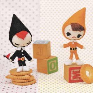 Peut inclure: Deux poupées en feutre, l'une en noir et rouge avec un drapeau, l'autre en orange avec un visage brun, debout sur des blocs de bois et un biscuit.