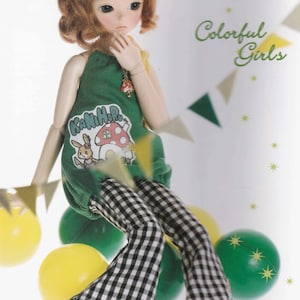 Puede incluir: Una muñeca con cabello castaño que lleva un atuendo a cuadros verde y blanco con un gráfico de hongo y conejo. La muñeca está rodeada de globos y confeti coloridos.