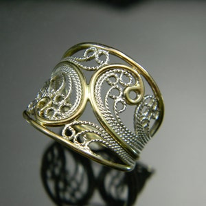 May include: A silver filigree ring with a gold band. The ring is made of delicate, intricate designs and is a beautiful piece of jewelry.