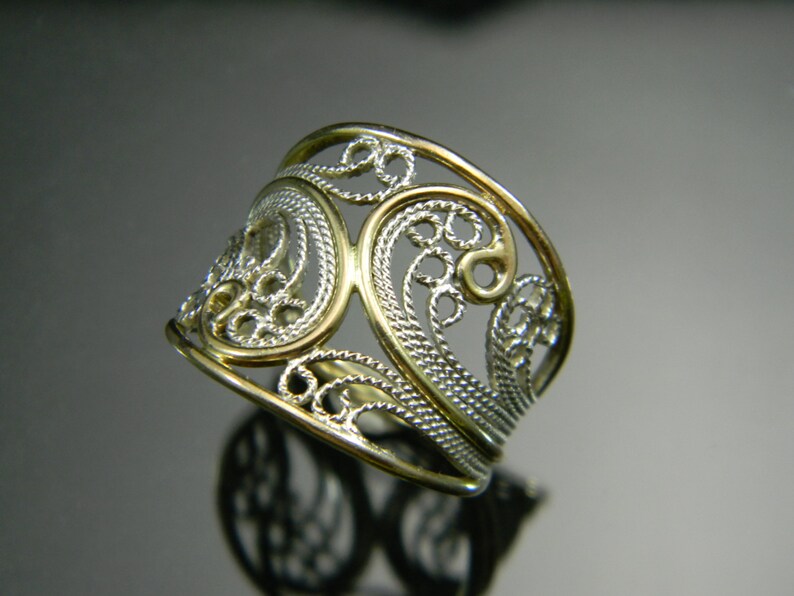 May include: A silver filigree ring with a gold band. The ring is made of delicate, intricate designs and is a beautiful piece of jewelry.