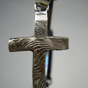 May include: Silver cross pendant with a textured surface. The pendant has a loop at the top for attaching to a chain.