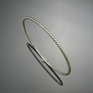 May include: A silver beaded bangle bracelet. The bracelet is thin and delicate, with a smooth, polished finish.