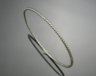 May include: A silver beaded bangle bracelet. The bracelet is thin and delicate, with a smooth, polished finish.