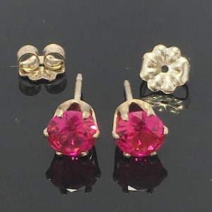 May include: A pair of gold stud earrings with pink gemstones. The earrings have a simple design and are perfect for everyday wear.