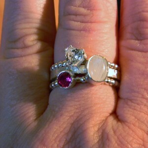 May include: A silver ring with three stones: a white round stone, a smaller white round stone, and a pink round stone.