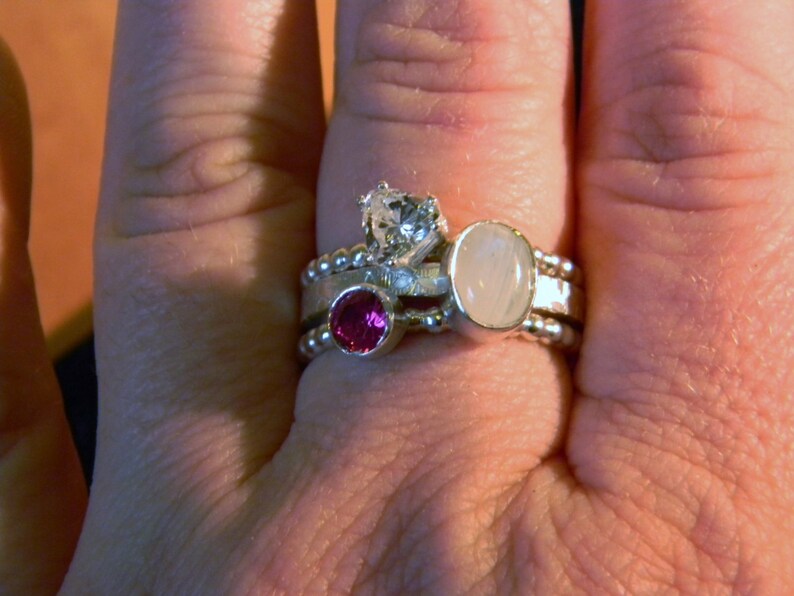 May include: A silver ring with three stones: a white round stone, a smaller white round stone, and a pink round stone.