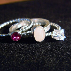 May include: Three silver rings with different gemstones. The first ring has a pink stone, the second ring has a white stone, and the third ring has a clear stone.
