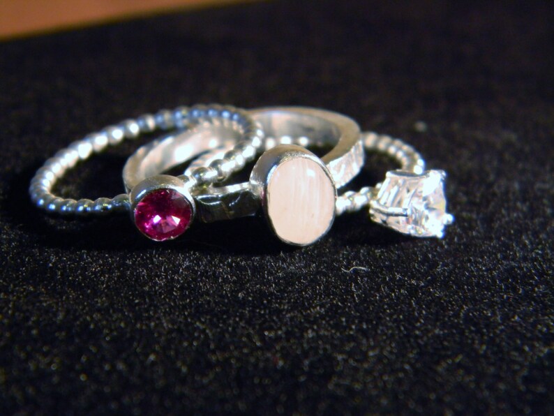 May include: Three silver rings with different gemstones. The first ring has a pink stone, the second ring has a white stone, and the third ring has a clear stone.