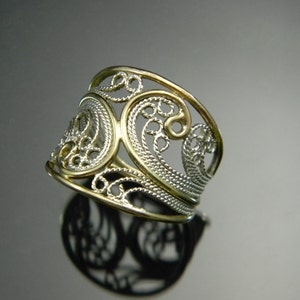 May include: A silver and gold filigree ring with a wide band and intricate design.