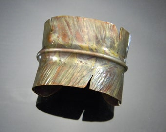 May include: A copper bracelet with a textured surface and a band around the middle. The bracelet has a worn, aged look.