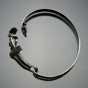 May include: A silver bracelet with a cross charm. The bracelet is made of a thin metal band and has a simple design.