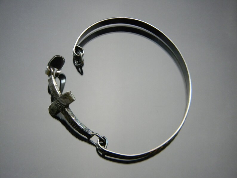 May include: A silver bracelet with a cross charm. The bracelet is made of a thin metal band and has a simple design.
