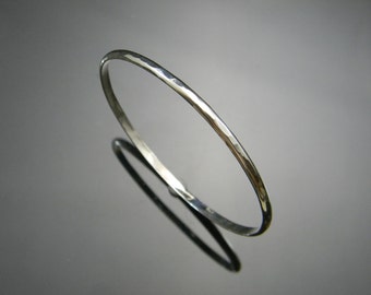 May include: A silver hammered bangle bracelet. The bracelet is thin and has a smooth, polished finish.