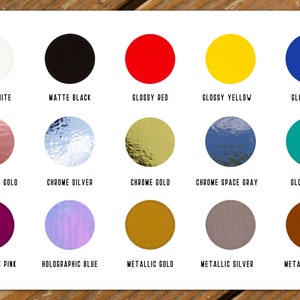 May include: A color palette featuring fifteen circular color swatches. Colors include glossy white, matte black, glossy red, yellow, and blue. Other colors are chrome rose gold, silver, gold, space gray, teal, holographic pink, blue, metallic gold, silver, and bronze.