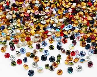Puede incluir: Surtido de piedras de imitación de colores en varias formas y tamaños, incluyendo redondas, cuadradas y en forma de estrella. Las piedras de imitación están esparcidas sobre un fondo blanco.