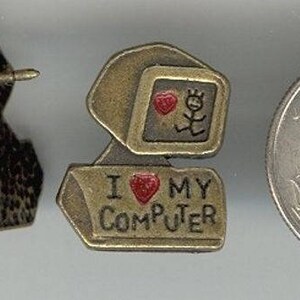 May include: A gold-toned pin with a computer monitor and the text "I love my computer". The pin has a red heart and a stick figure with a red heart. The pin is attached to a silver-toned pin back.
