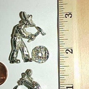 May include: Two silver-colored figurines of people holding tools. The figurines are about 2 inches tall and are standing on a white surface.
