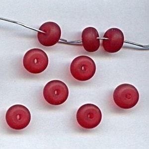 May include: Ten red glass beads with a frosted finish. The beads are round and have a hole in the center. The beads are about the size of a US penny.