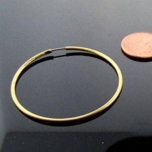 May include: A pair of gold hoop earrings. The earrings are large and circular, and they are shown against a black background.