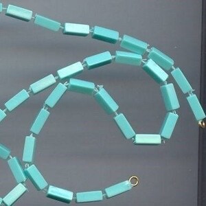 May include: A turquoise blue necklace made of rectangular beads. The necklace is strung on a thin wire and has a gold clasp.