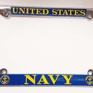 May include: A chrome licence plate frame with a blue and yellow design. The frame features the words "UNITED STATES NAVY" and an anchor emblem.