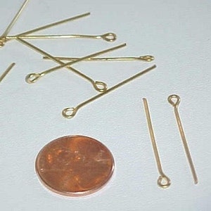 May include: A group of gold-colored head pins with a loop at the end. The pins are scattered on a white surface next to a US penny.