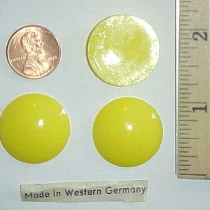 May include: Four yellow plastic buttons with a shiny finish. The buttons are approximately 1 inch in diameter. A ruler is in the background for size reference. The buttons have the text "Made in Western Germany" printed on a label below them.