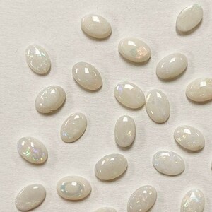 May include: A collection of oval-shaped white opal gemstones with iridescent flashes of color.