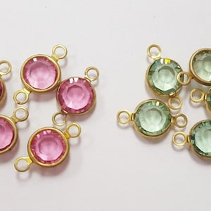 May include: A set of 10 gold-tone metal connector charms with faceted glass stones. Five charms have pink stones and five charms have light green stones.