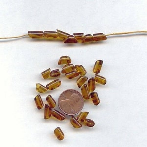 May include: A pile of amber glass beads, some are rectangular and some are triangular, next to a US penny.