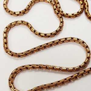 May include: A gold chain necklace with a box chain design. The chain is made of metal and has a shiny finish.