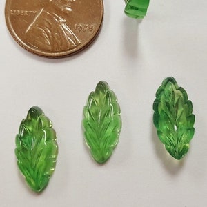 May include: Four green carved glass leaves, each with a different vein pattern. The leaves are approximately the size of a US penny.