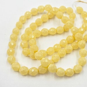 May include: A strand of pale yellow faceted glass beads. The beads are strung on a white thread and are arranged in a loose circle.