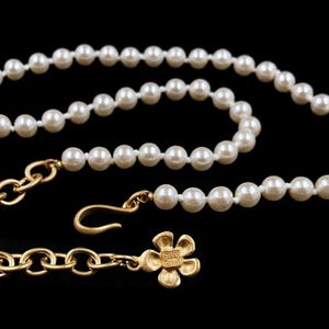 May include: A white pearl necklace with a gold chain and a flower charm. The charm has the text "Give Gift" on the back.
