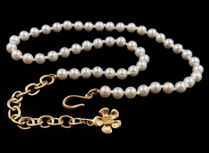 May include: A white pearl necklace with a gold chain and a flower charm. The charm has the text "Give Gift" on the back.