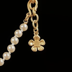 May include: A gold chain necklace with a flower charm and a strand of white pearls.