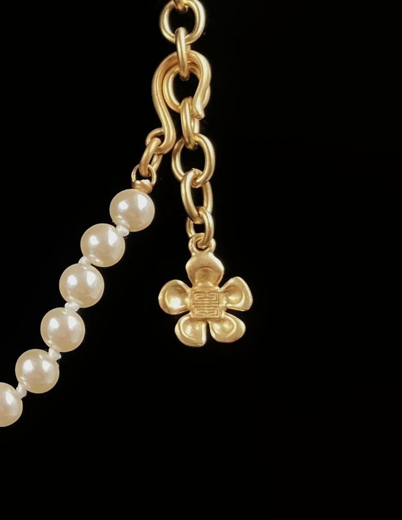 May include: A gold chain necklace with a flower charm and a strand of white pearls.