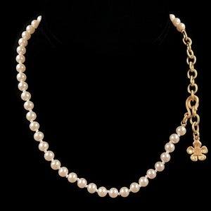 May include: A white pearl necklace with a gold chain and a small gold flower charm.