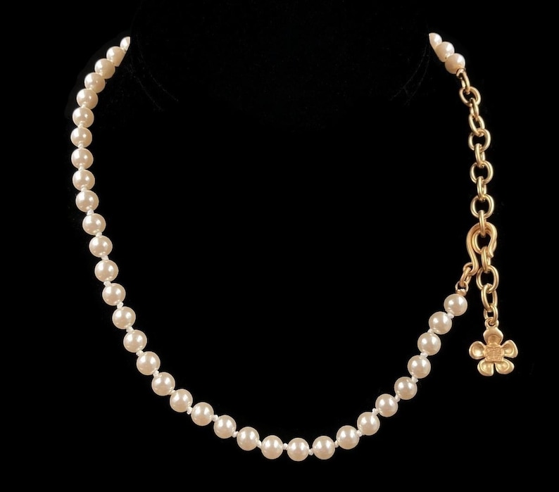 May include: A white pearl necklace with a gold chain and a small gold flower charm.