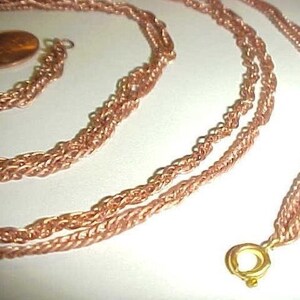 Könnte beinhalten: Eine lange, roségoldene Kettenkette mit einem goldenen Verschluss. Die Kette besteht aus mehreren Strängen verdrillten Drahtes.