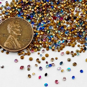 May include: A close-up image of a variety of colorful rhinestones and gold-toned metal beads. The beads are scattered on a white surface. A US penny coin with the year 1962 is visible in the image.