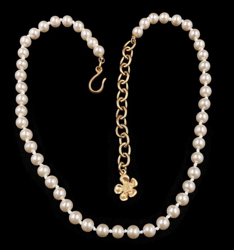 May include: A white pearl necklace with a gold chain extender and a small gold flower charm.